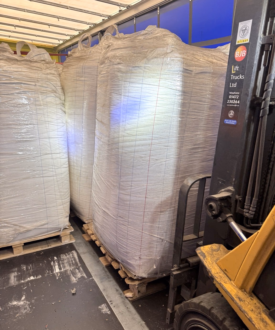A forklift handling large wrapped bulk bags inside a trailer