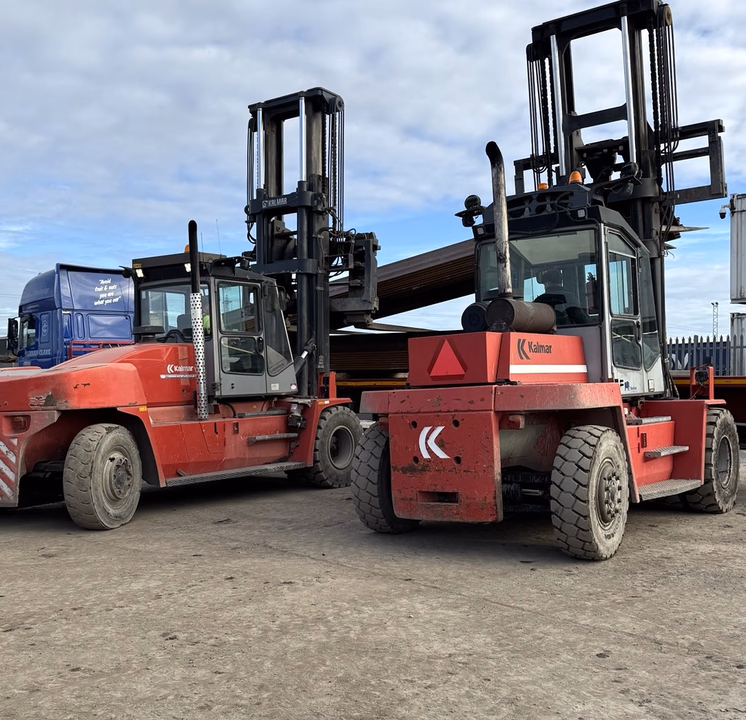 Two red Kalmar heavy-duty forklifts parked side by side in the yard