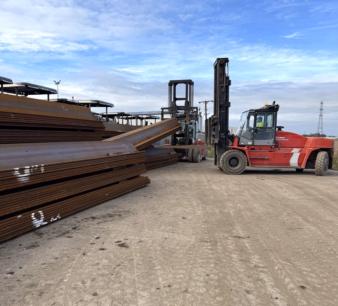 Steel sheet piles stacked in the yard with Kalmar heavy-duty forklifts behind