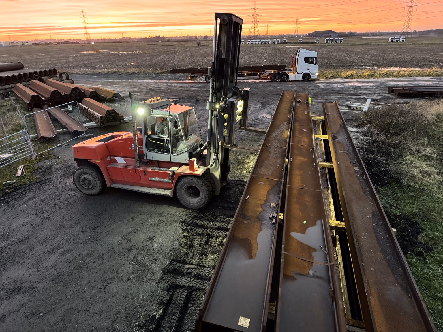 A Kalmar heavy-duty forklift working beside long steel sections under an orange sky