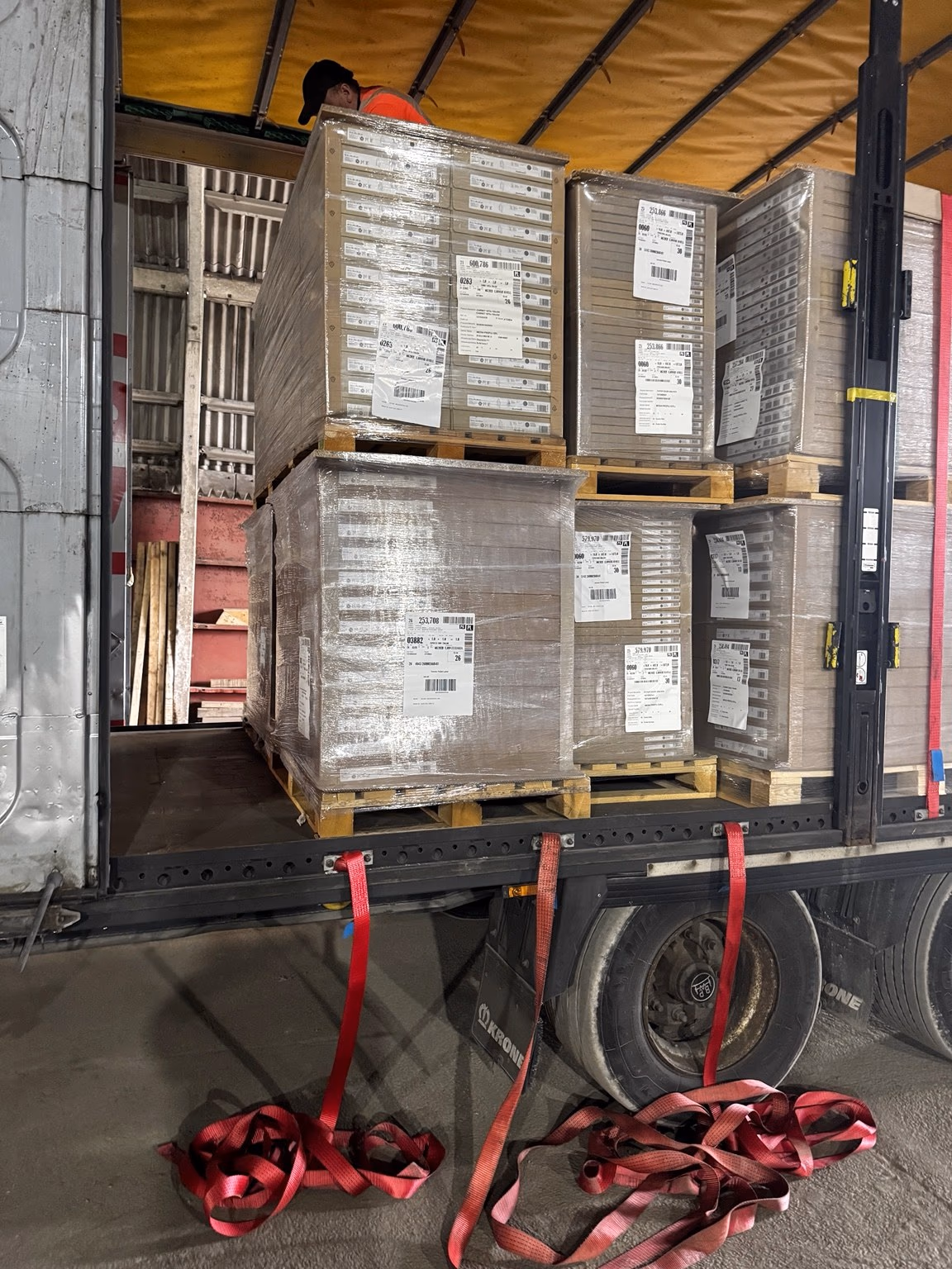 Pallets loaded on a curtain-sided trailer inside the warehouse, with straps ready to secure the load
