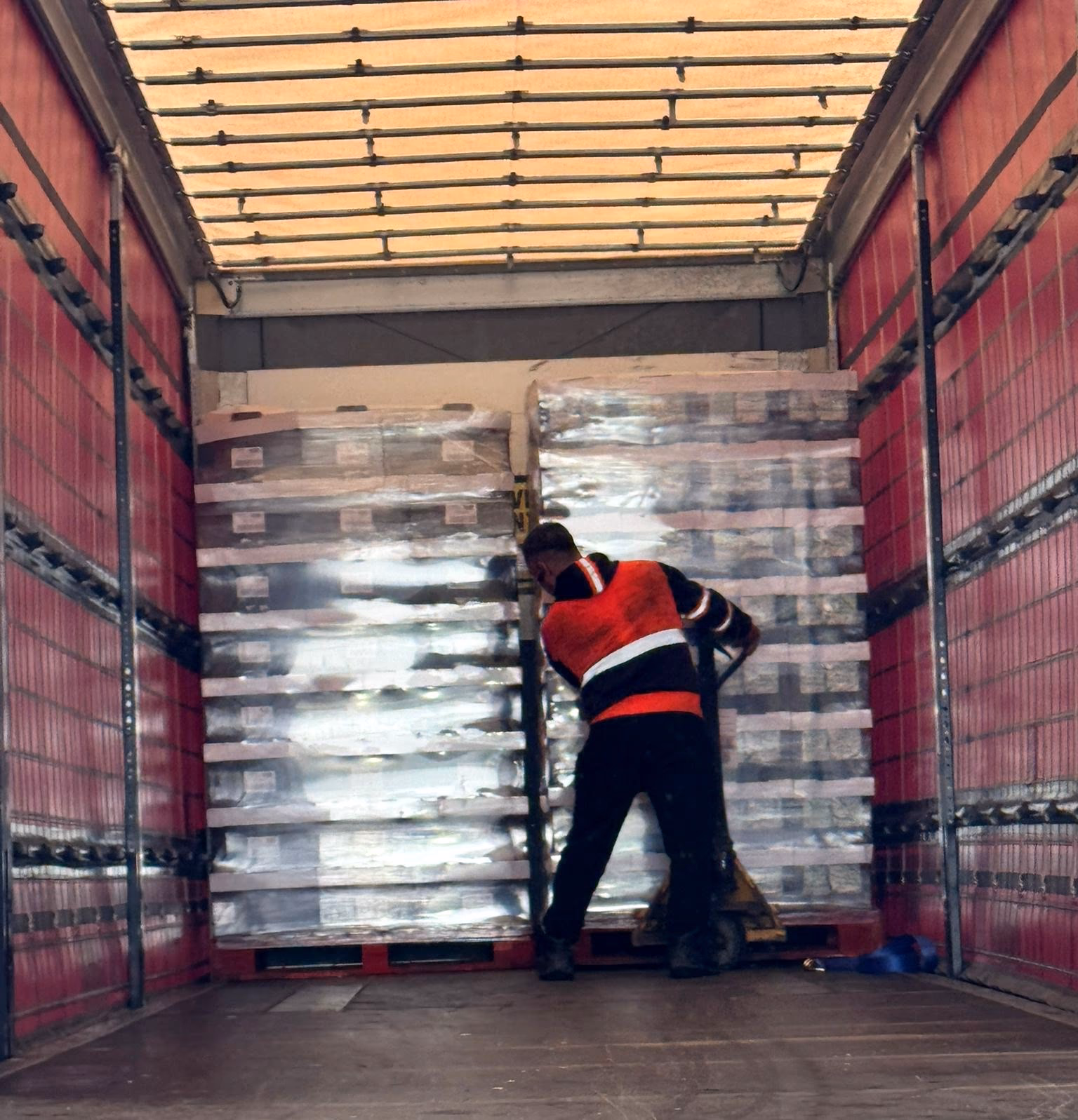 An MLK operator moving a wrapped pallet inside a curtain-sided trailer with a pallet truck