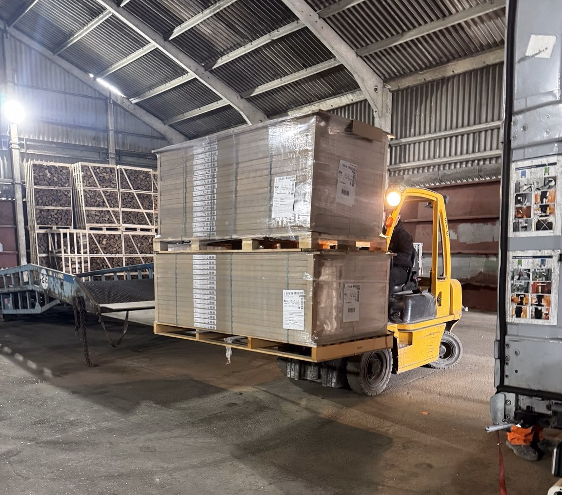 A forklift lifting two stacked pallets of boxed goods inside the MLK warehouse